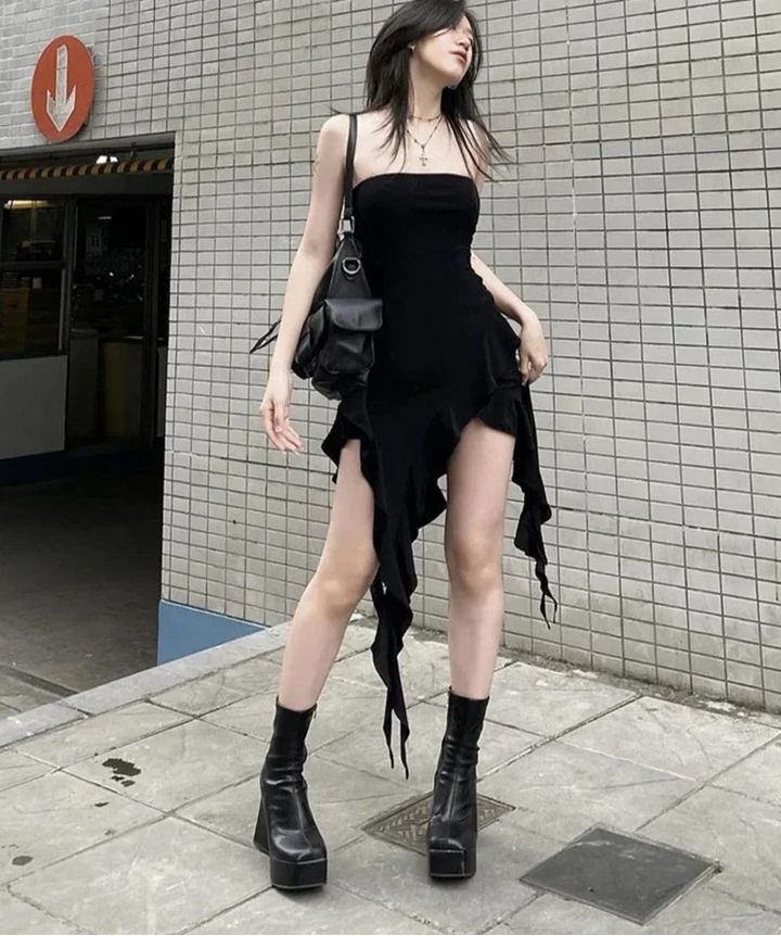 Woman in a black dress and boots standing against a tiled wall.
