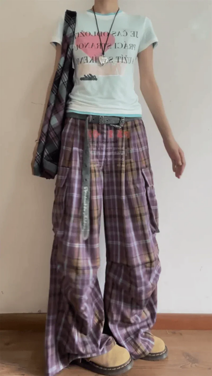 Person wearing a light-colored t-shirt with text and plaid pants against a plain background