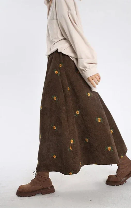 Person wearing a brown skirt with floral embroidery on a white background