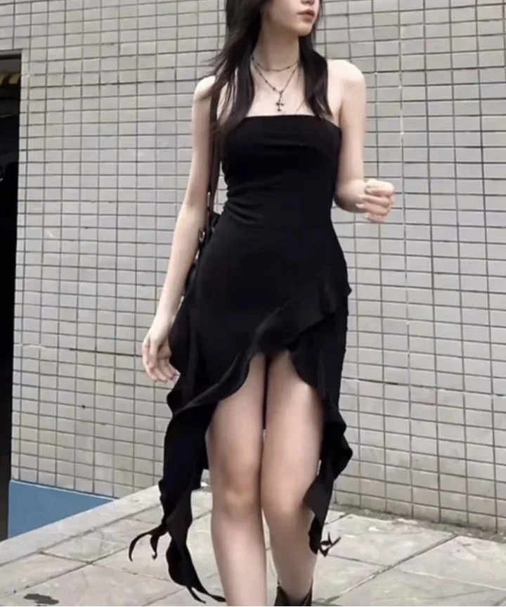 Woman wearing a black dress with a high slit standing against a tiled wall.