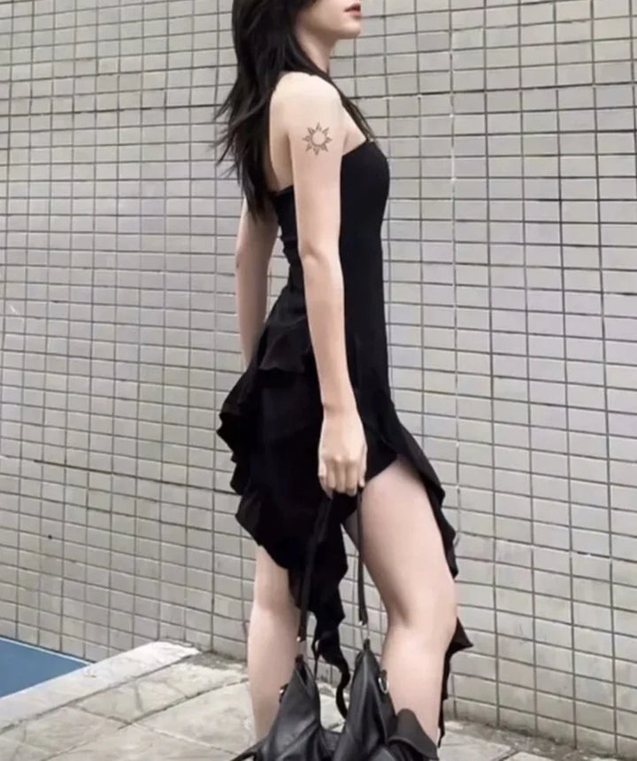 Woman wearing a black dress with ruffled details against a tiled wall.