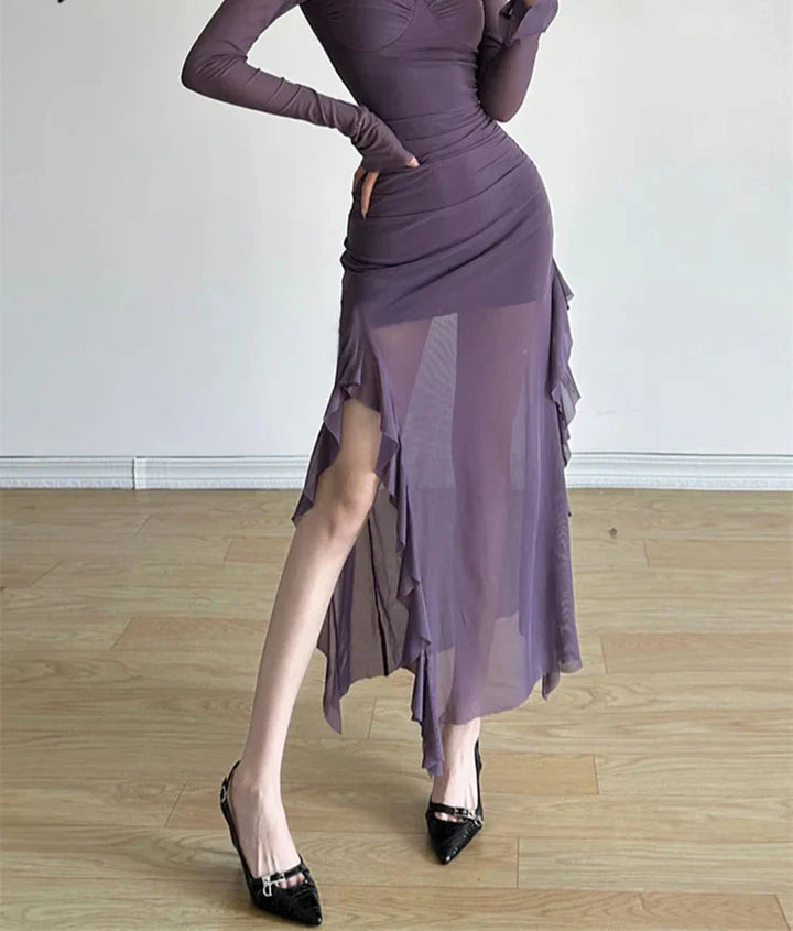 Woman wearing a long-sleeve purple dress with a slit on a wooden floor.